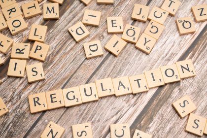 Peças de madeira formam a palavra “Regulation” sobre uma superfície texturizada, remetendo à regulamentação de criptoativos.